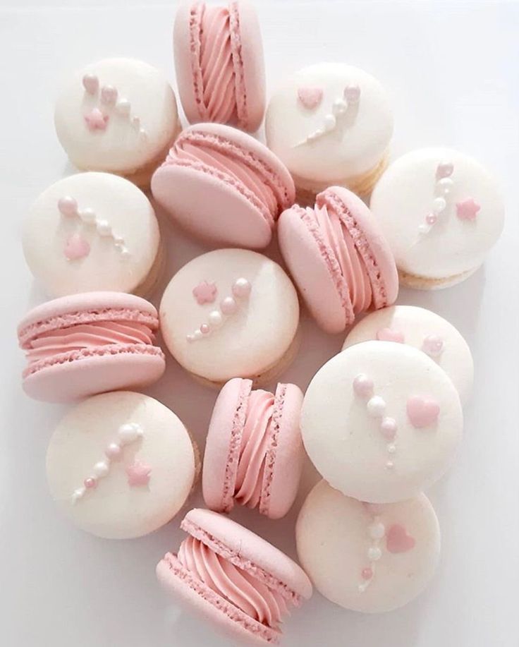 there are many pink and white macaroons on the table, one is decorated with icing