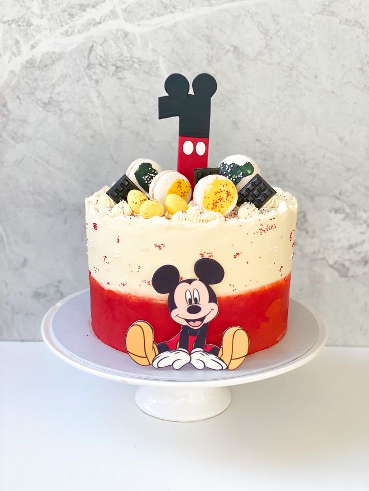 a mickey mouse cake on a white plate with a red and yellow frosting top