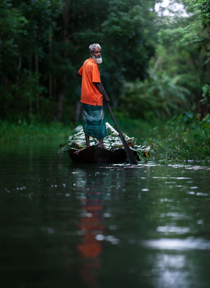 a man standing on top of a boat in the middle of a river surrounded by trees