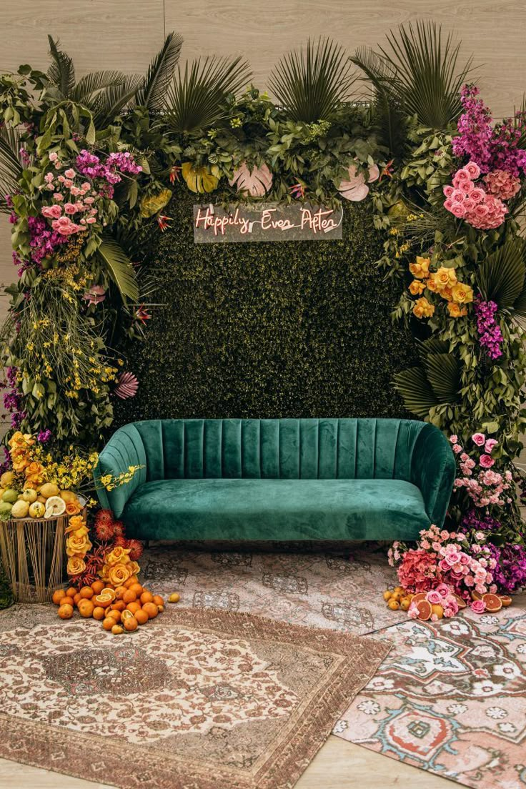 a green velvet couch sitting in front of a wall with flowers and greenery on it