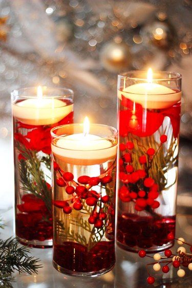 three candles with red berries and greenery in them on a table next to christmas decorations