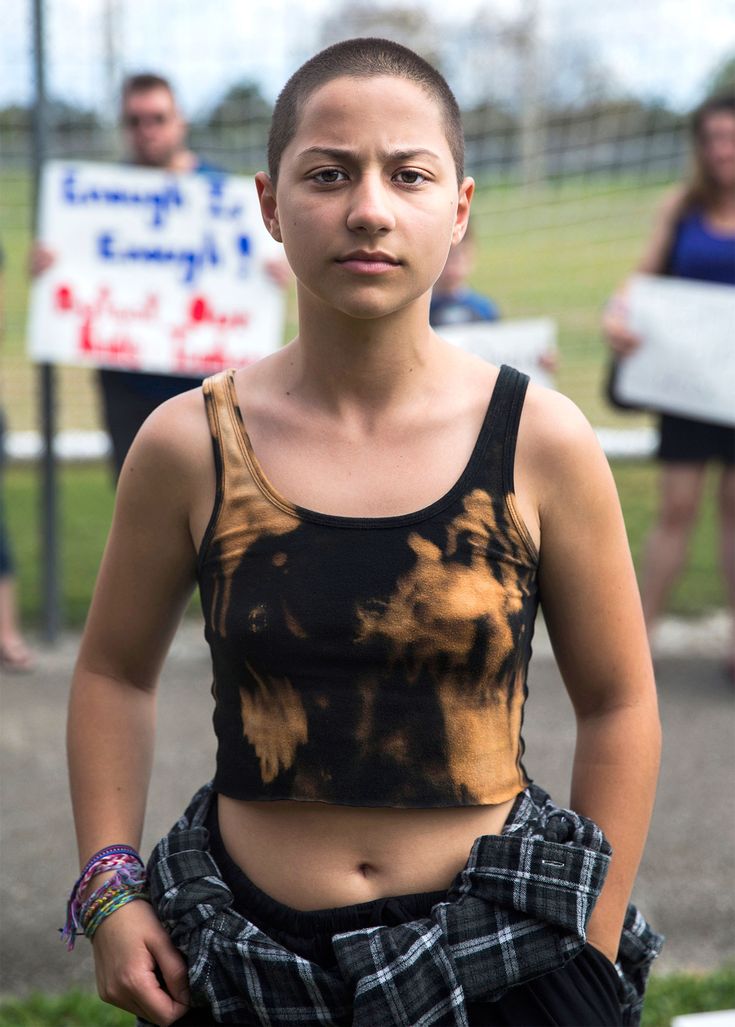 a young woman standing in the grass with her hands on her hips and people holding signs behind her