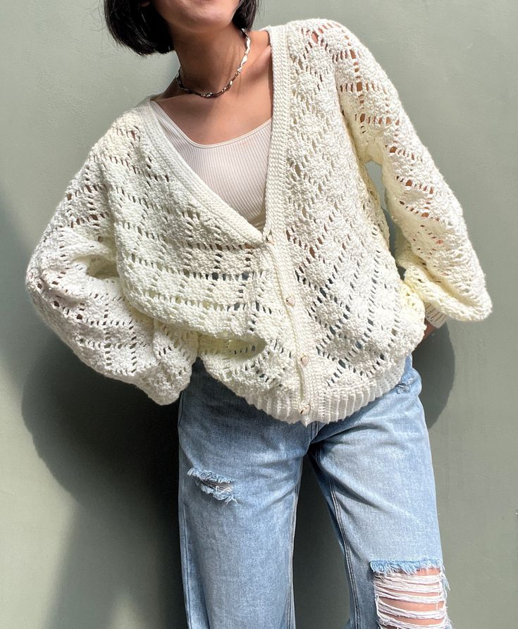 a woman standing against a wall with her hands on her hips wearing ripped jeans and a white knitted sweater