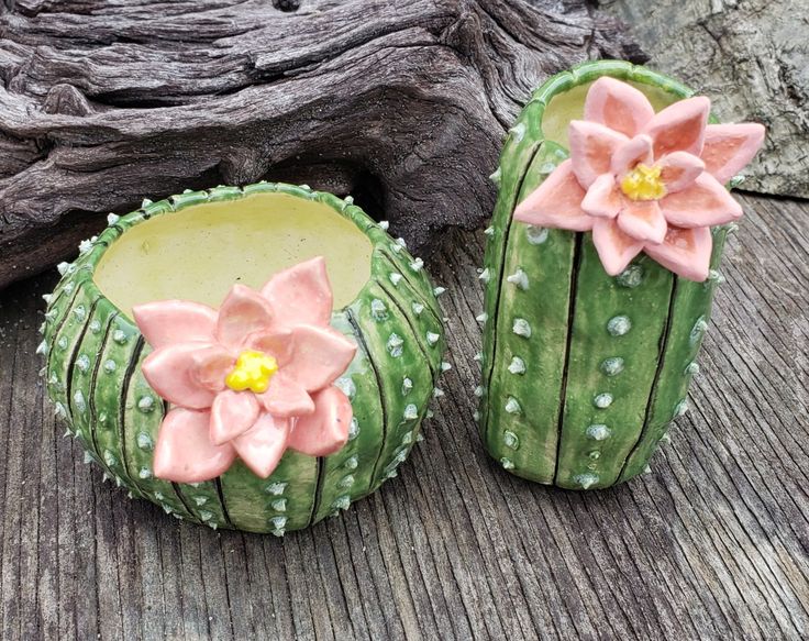 two cactus shaped cupcakes with flowers on them sitting next to a tree trunk