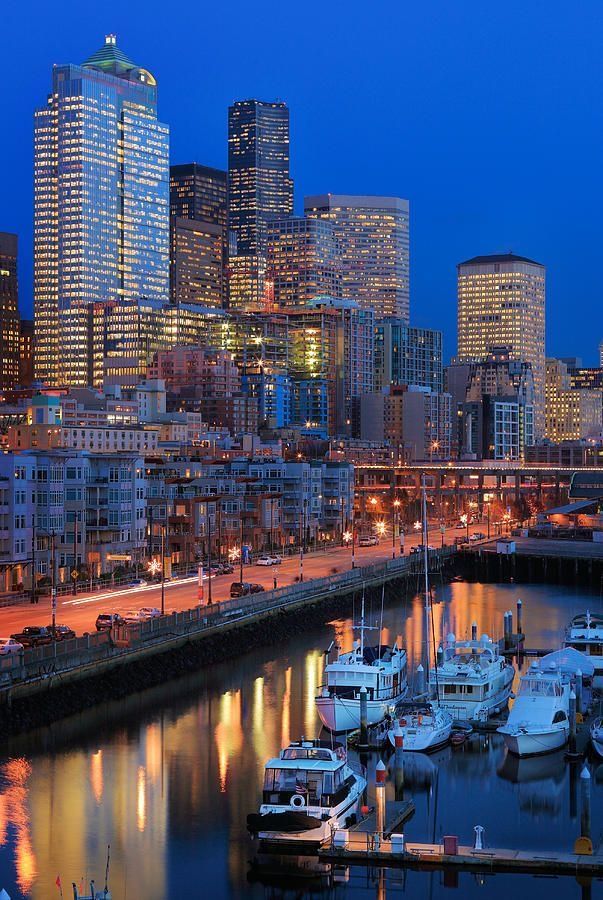 the city skyline is lit up at night, with boats docked in the harbor below