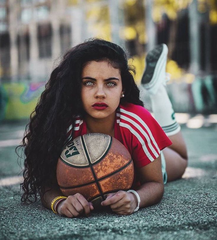 a woman laying on the ground with a basketball in her hand and looking at the camera