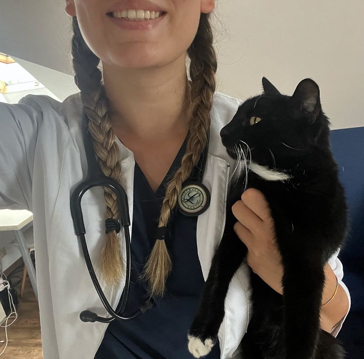 a woman in a white lab coat holding a black and white cat while wearing a stethoscope