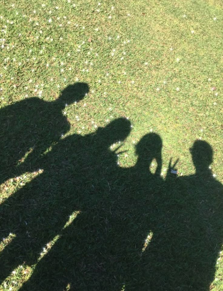 the shadow of three people standing on top of a grass covered field next to a frisbee