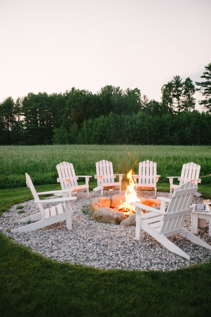 a fire pit with chairs around it in the middle of a grassy field at dusk