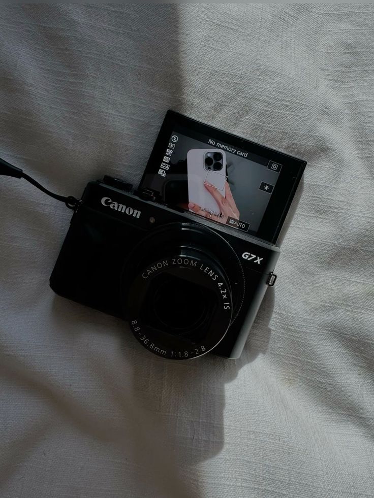 a camera sitting on top of a bed next to a white sheet with a cell phone