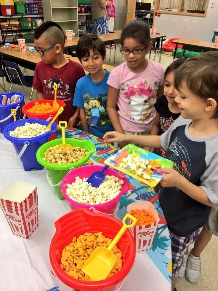 several children standing around a table with buckets of food on it and popcorn in front of them