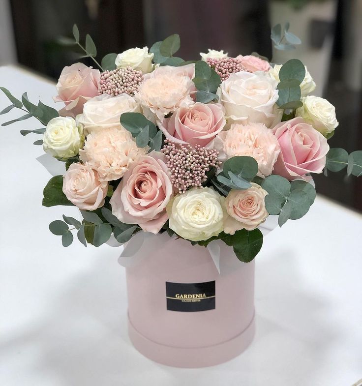 a pink and white flower arrangement in a round vase on a table with greenery