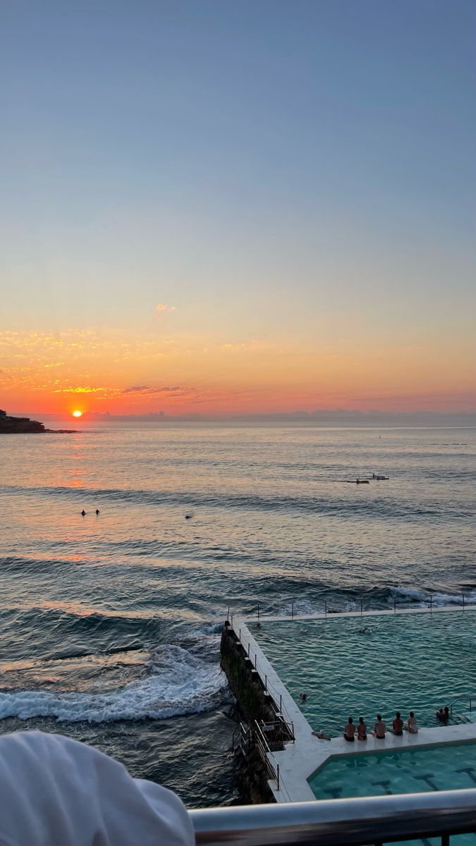 the sun is setting over an ocean with people swimming