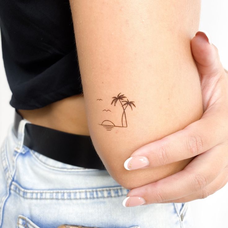 a woman's arm with a small palm tree tattoo on the left side of her right arm