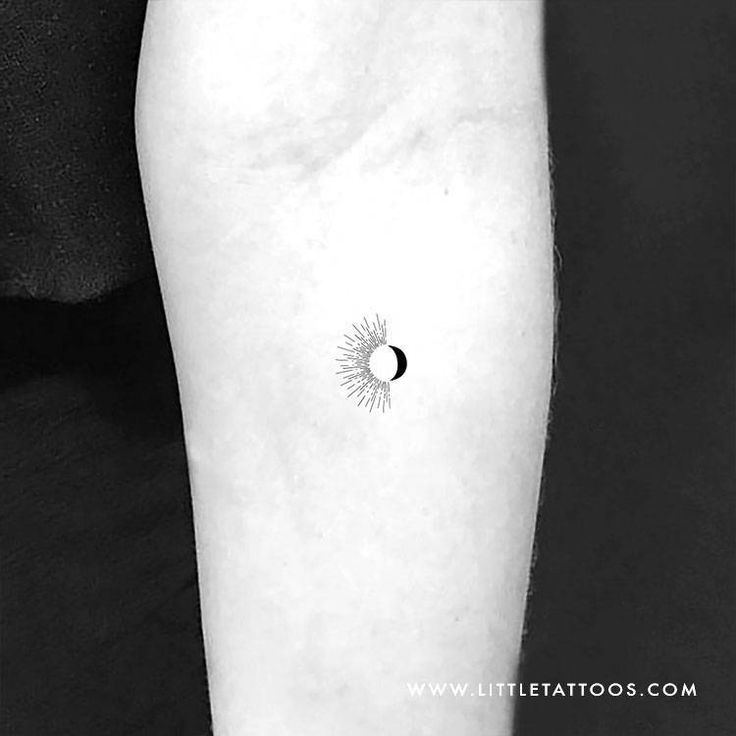 a black and white photo of a person's arm with a small sun tattoo on it