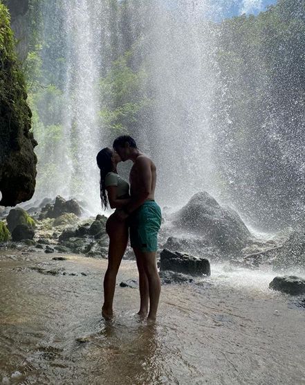 two people standing in front of a waterfall with their arms around each other and kissing