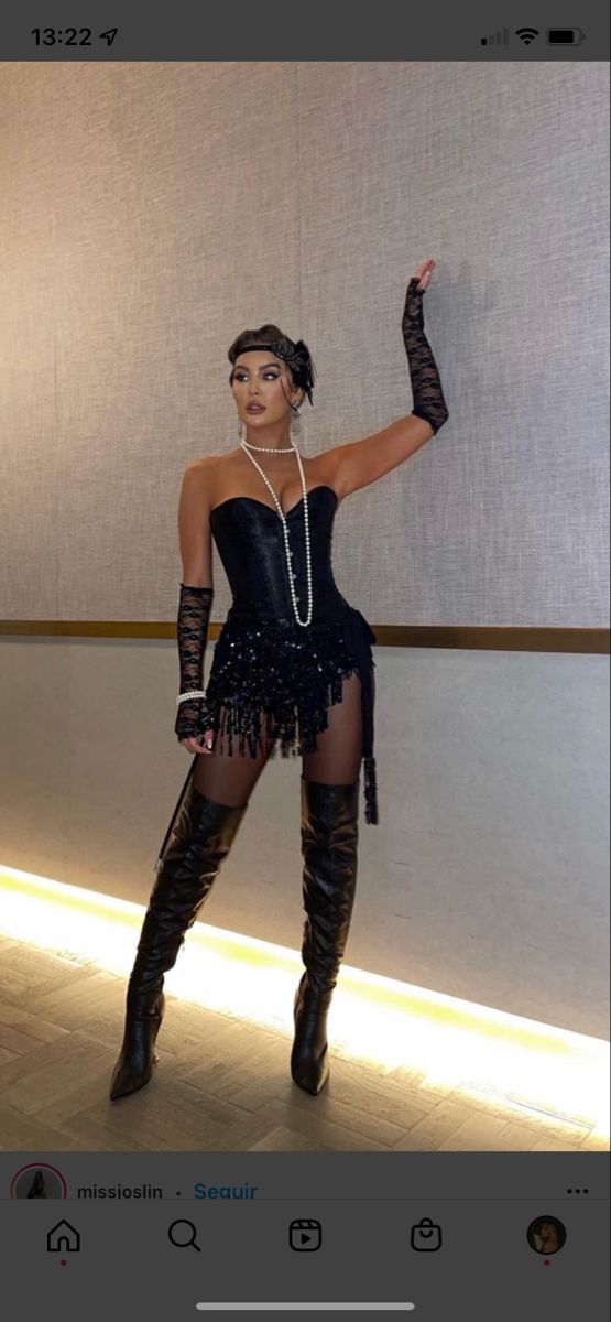 a woman in a black dress and thigh high boots posing for the camera with her hand up