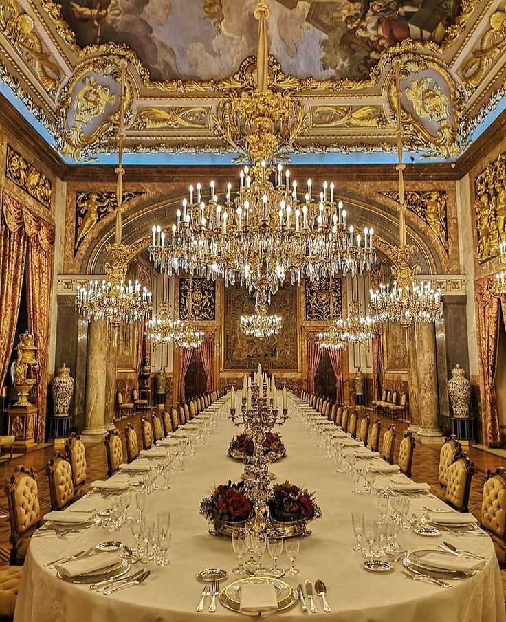 a fancy dining room with chandeliers and paintings on the ceiling is set for a formal dinner