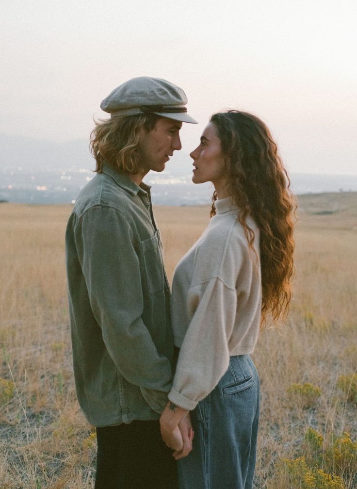 a man and woman are standing in the middle of an open field looking into each other's eyes