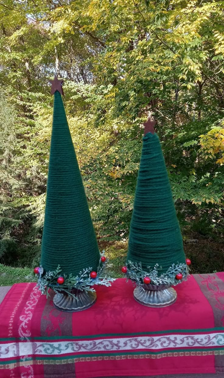 two green christmas trees sitting on top of a red and white table cloth in front of some trees