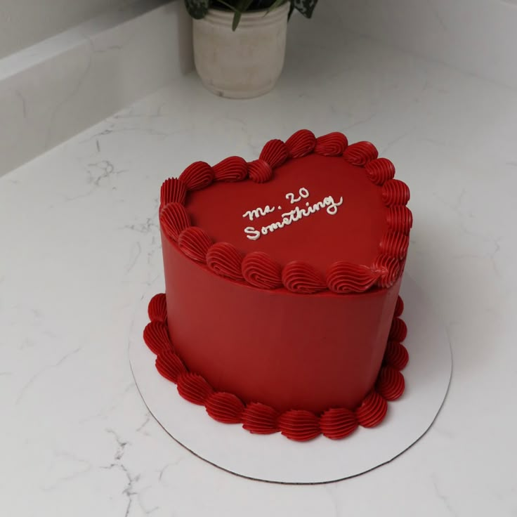 a red heart shaped cake sitting on top of a white counter next to a potted plant