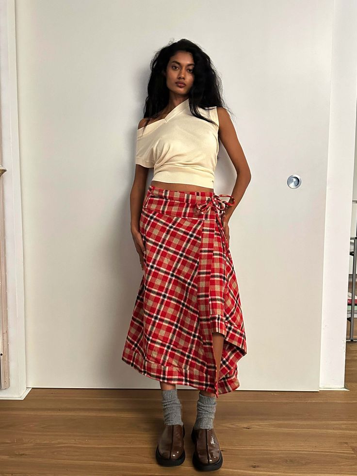 a woman standing in front of a white wall wearing a red and black plaid skirt