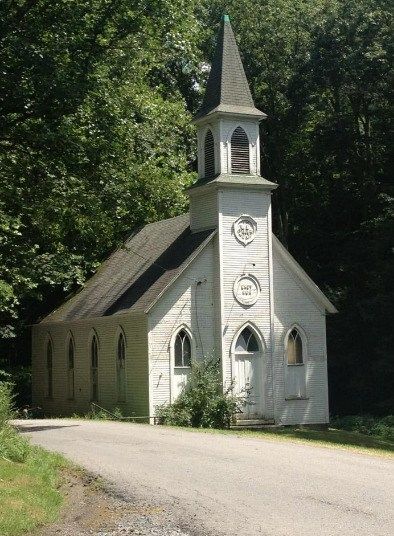 an old white church with a steeple surrounded by trees