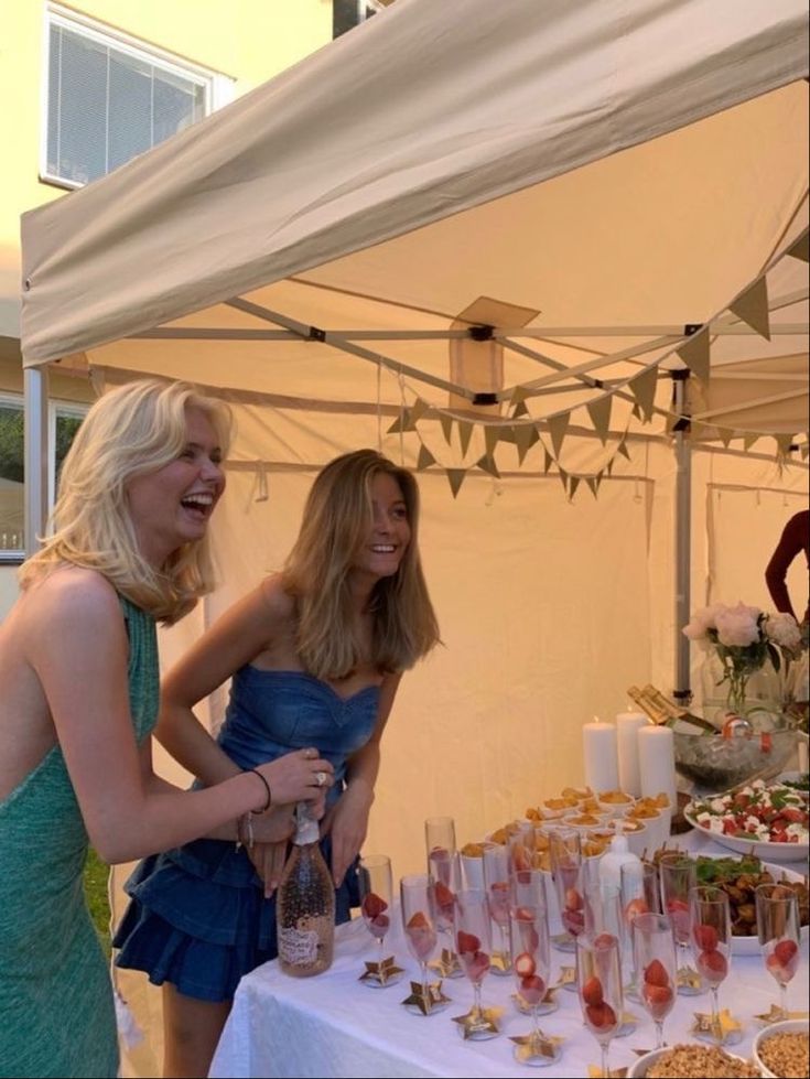 two women standing next to each other near a table full of desserts and drinks