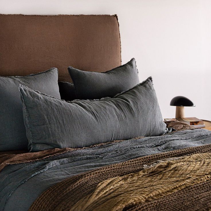 a bed with two pillows on top of it next to a night stand and lamp