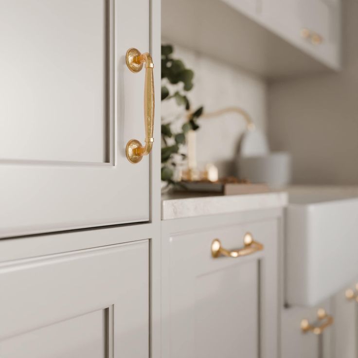 a kitchen with white cabinets and gold handles on the doors, in front of a potted plant