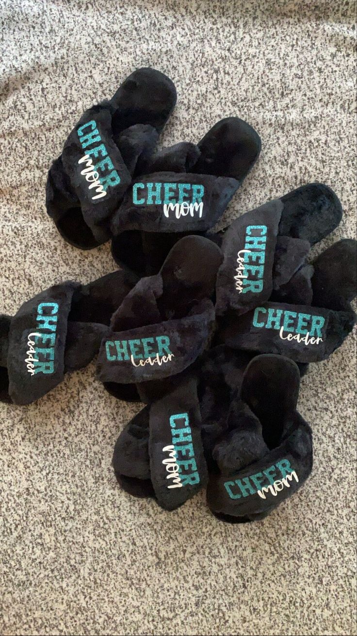 several pairs of black slippers with the word cheer written on them sitting on a carpeted floor