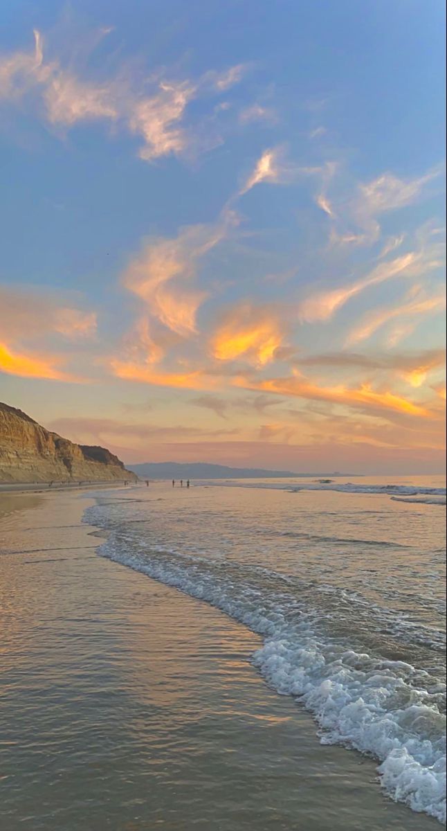 the sun is setting at the beach with people walking in the water and on the sand