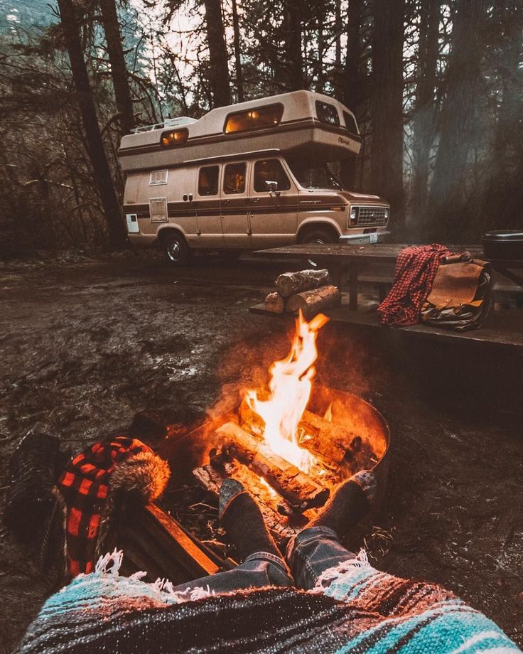 a camper sitting in front of a fire with his feet up on the ground