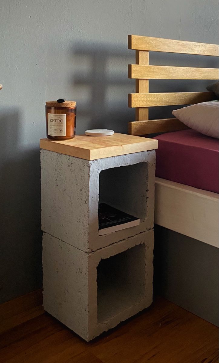 a bed with a wooden headboard next to a cement block table and shelf on the floor