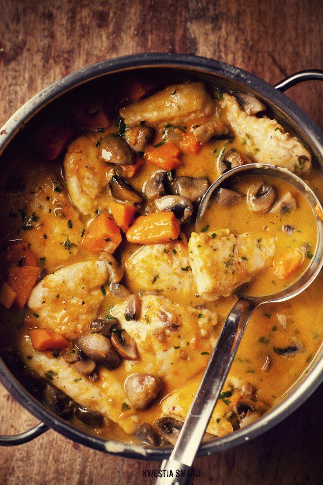 a pot filled with chicken, mushrooms and carrots next to a spoon on top of a wooden table