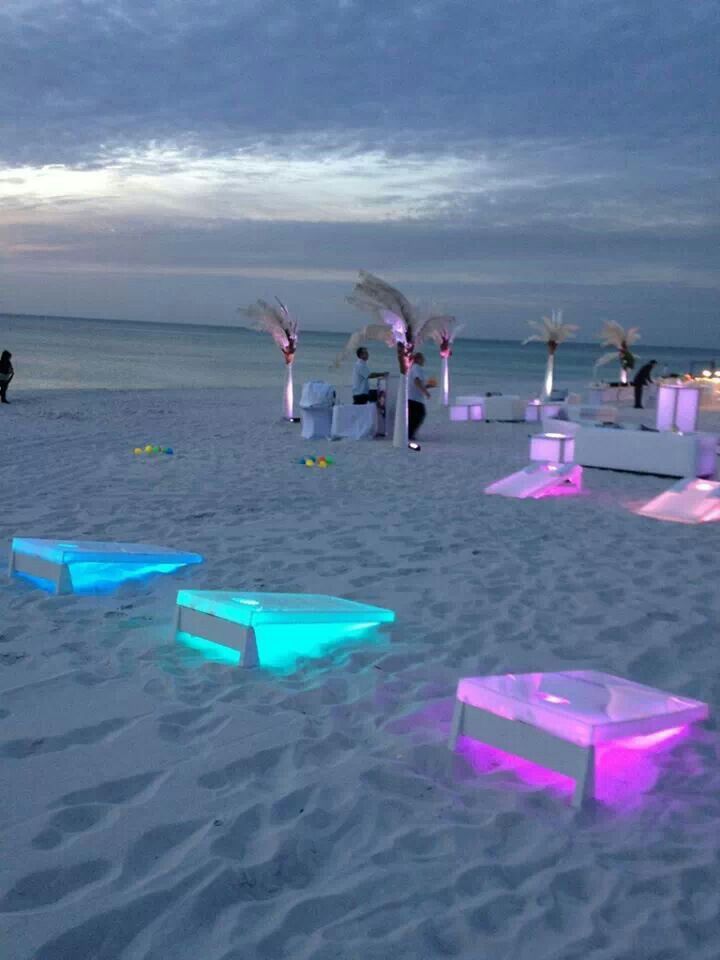 an outdoor event set up on the beach at night with colorful lights and chairs in the sand