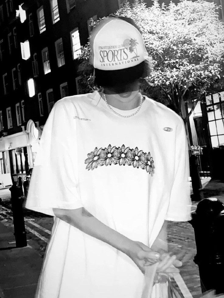 a person wearing a t - shirt and hat standing on the sidewalk in front of a building