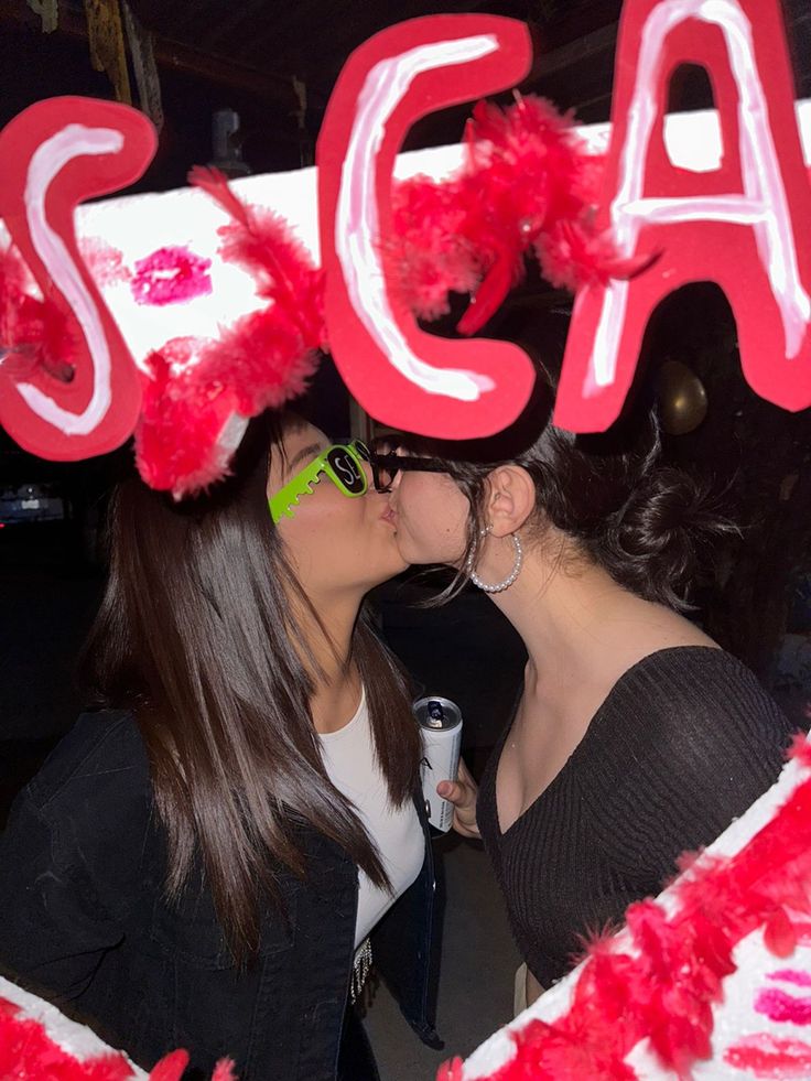 two women kissing each other in front of a sign that says scaf on it