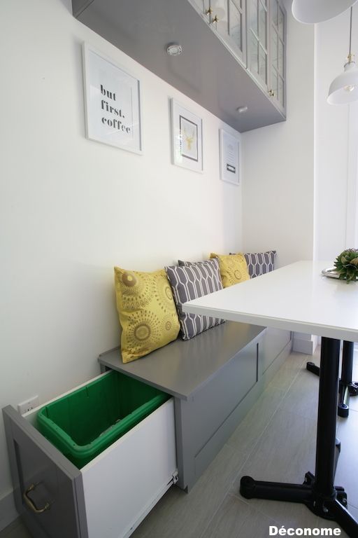 a white table sitting under a window next to a bench with yellow pillows on it