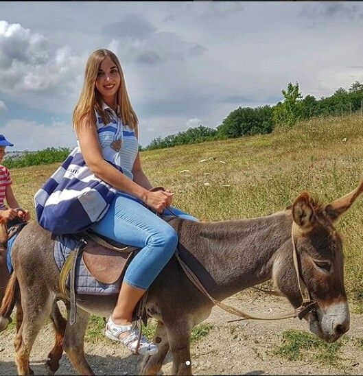 two people riding donkeys down a dirt road with grass and trees in the background