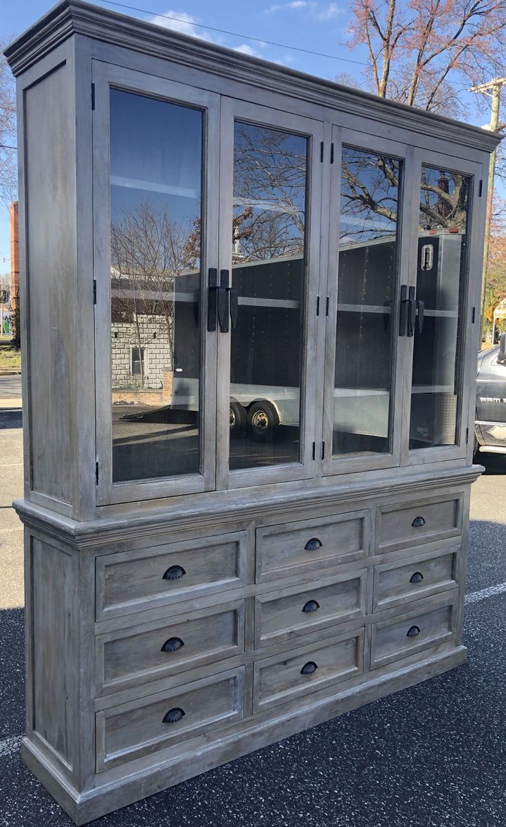 an old gray china cabinet with glass doors on the top and bottom, sitting in a parking lot