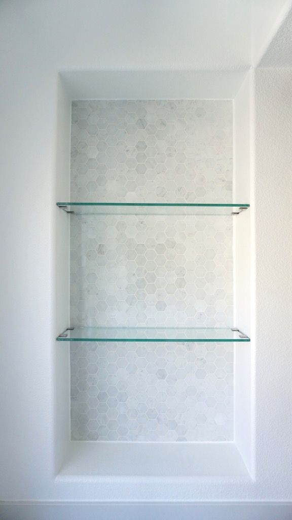 three glass shelves in the corner of a white room with hexagonal tiles on the wall