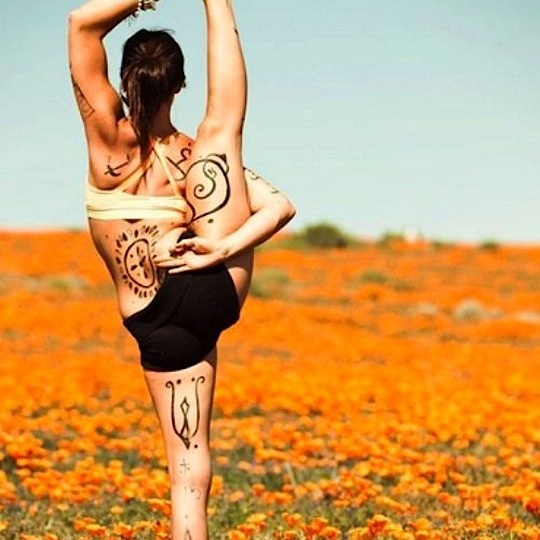 a woman standing on one leg in the middle of a flower field with her arms up