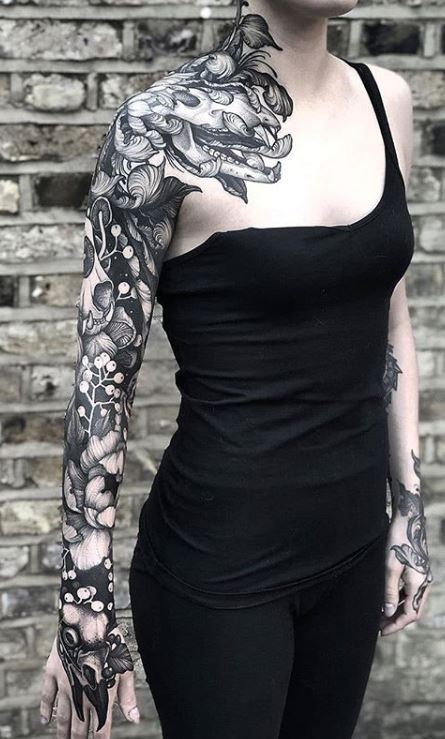 a woman with tattoos standing in front of a brick wall