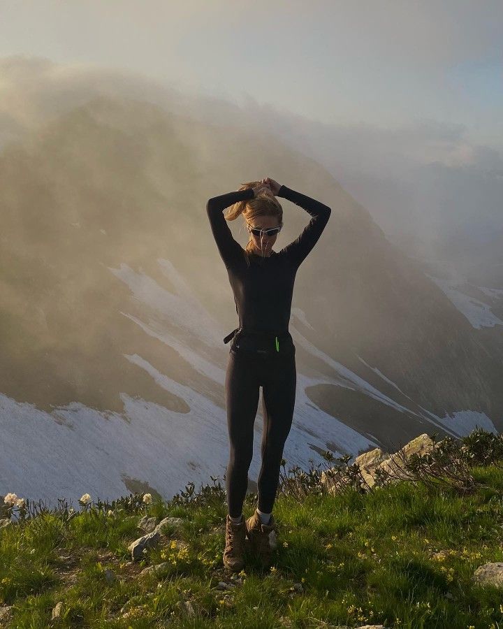 a woman standing on top of a lush green hillside