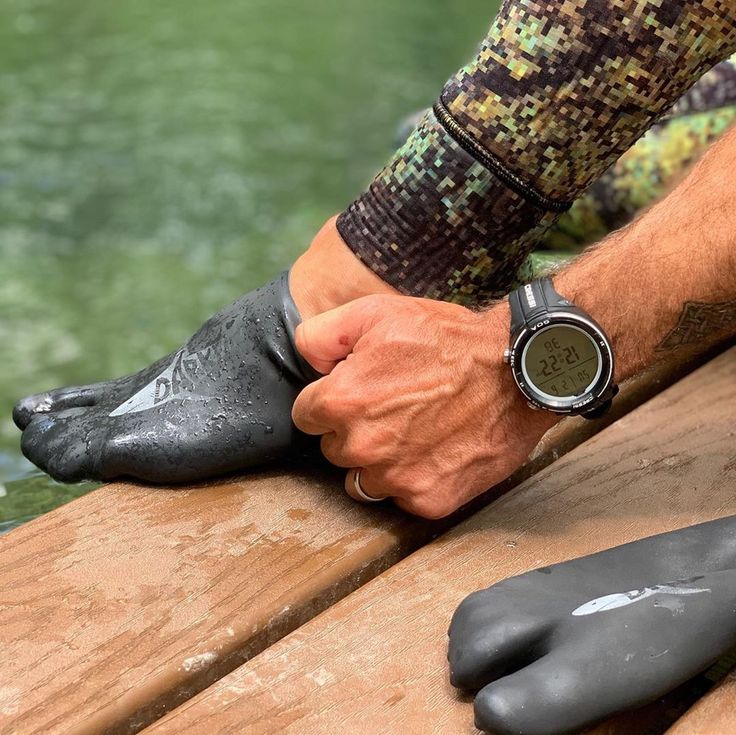 a man with his foot on the edge of a body of water wearing wetsuits and rubber shoes