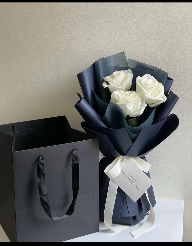 a bouquet of white roses sitting on top of a table next to a black bag