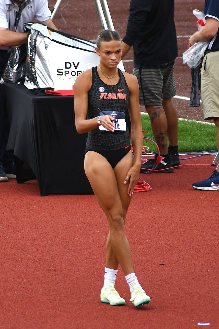 a woman in a black swimsuit is standing on a red track with other people behind her