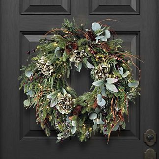 a wreath on the front door of a house decorated with greenery and pine cones