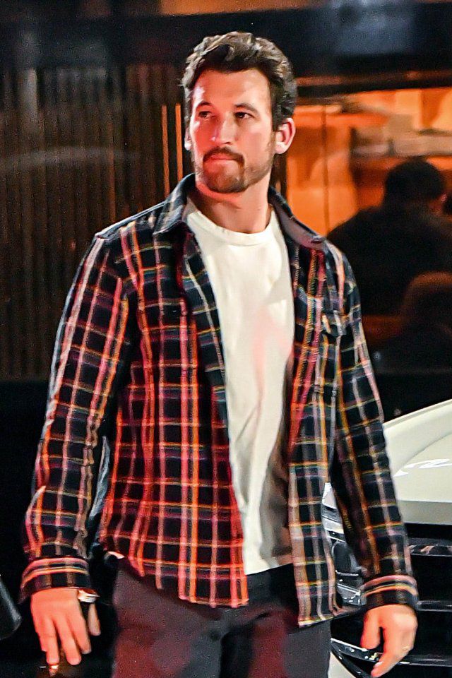 a man walking down the street with his hand in his pocket and wearing a plaid jacket